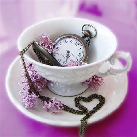 A White Cup Filled With Purple Flowers And A Pocket Watch On Top Of The Cup