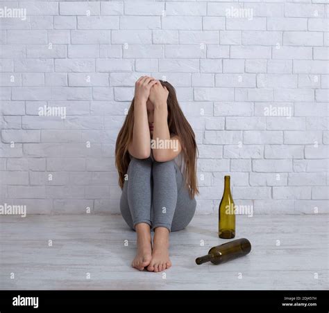 Alcoholism And Depression Concept Young Woman Crying On Floor At Home With Empty Bottles Around