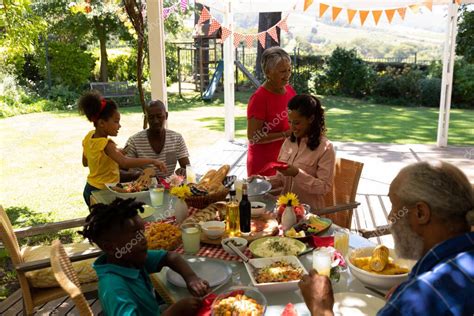 Vista Lateral De Una Familia Multiétnica Y Multigeneracional Sirviendo Comida Sentados En Una