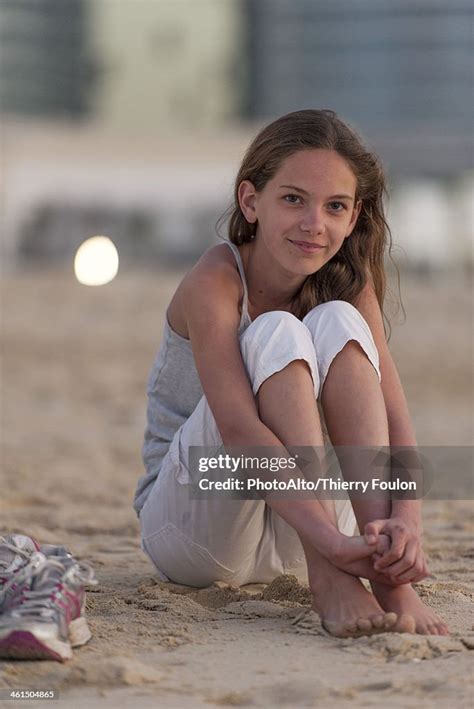 Preteen Girl Sitting On Beach With Barefeet Hugging Knees High Res