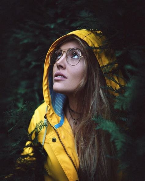 A Woman Wearing Glasses And A Yellow Raincoat Is Standing In Front Of Some Trees