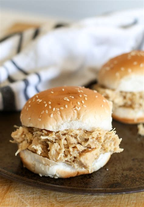 This shredded chicken sandwich is topped with tangy white sauce and crunchy pickles. Shredded Chicken Sandwiches In the Crockpot - Cleverly Simple