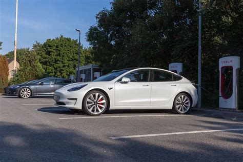Electric Car Tesla Model 3 Parks In The Shade In Front Of Supercharger