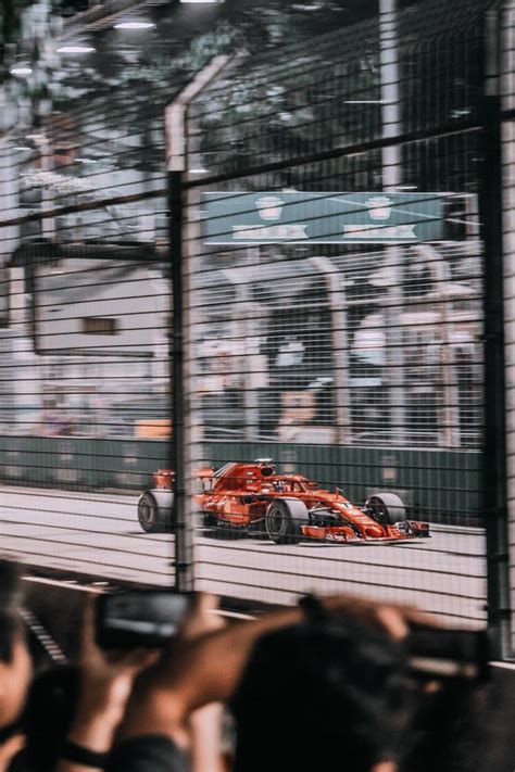 A Red Race Car Driving Down The Track In Front Of People On Their Cell