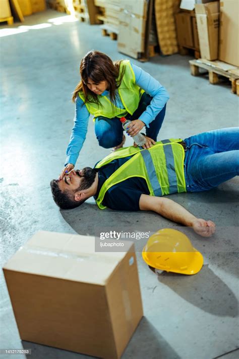 Warehouse Worker Helping Unconscious Worker Lying At Industrial Factory