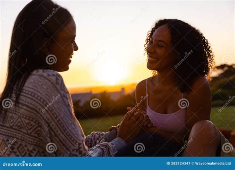 biracial lesbian couple sitting and holding hands in garden at sunset stock image image of