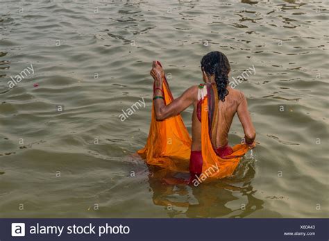 frau trägt einen orangefarbenen sari in baden in der sangam dem zusammenfluss der flüsse ganges