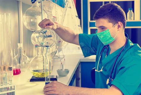 Male Scientist In Uniform Wearing A Mask Is Holding Test Glass A Stock