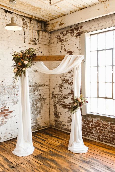 The Wedding Arch Is Decorated With Greenery And White Draping Along