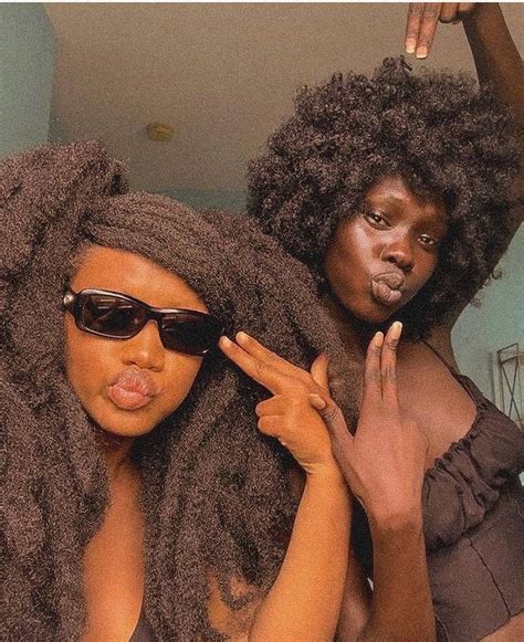 Two Women With Large Afros Are Posing For The Camera And One Is Brushing Her Hair