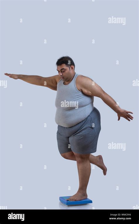 Obese Man Balancing On Weighing Scale With One Leg With His Hands