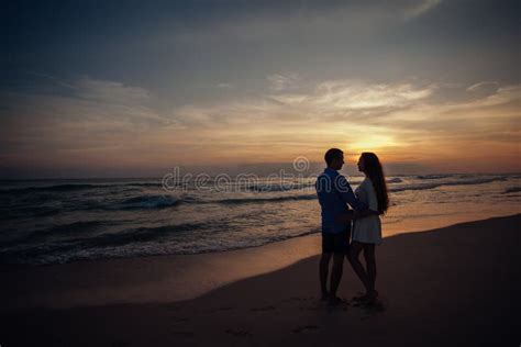 Two Young Lovers Standing On A Beach And Looking To Each Other On