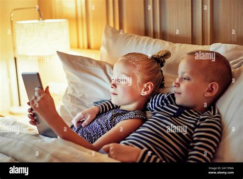 Cute Little Brother And Sister Lying In Bed Watching Something On A