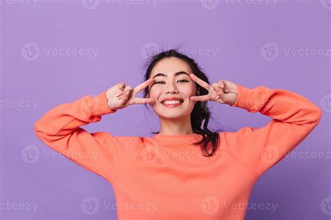 cheerful japanese girl showing peace signs laughing asian female model gesturing on purple