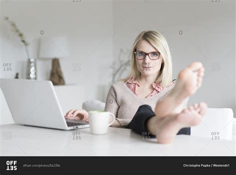 Portrait Of Blond Woman At Home Sitting At Table With Feet Up Stock