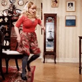 A Woman In A Red Dress Is Dancing On A Rug Near A Table And Chair