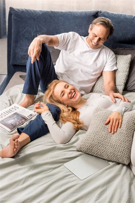 Middle Aged Couple Laughing And Lying On Bed At Home Stock Image