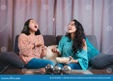 mom and daughter watching a movie at home they both make expressions when watching tv and eat