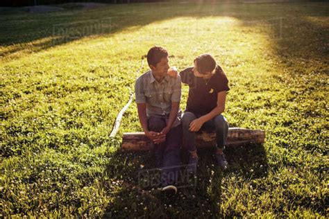 Father And Daughter Talking While Sitting On Log Amidst Grassy Field At