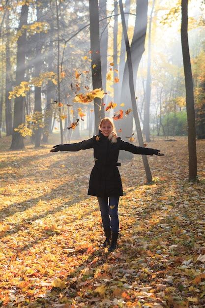 Premium Photo Redhead Girl Throws Up Autumn Leaves Under Bright Sunbeams In The Hazy Morning