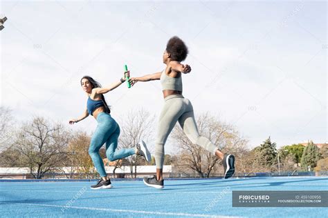 Fit Multiracial Female Athletes Passing Baton While Running Along Track
