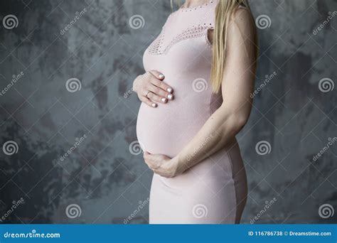 donna bionda incinta in un vestito leggero che abbraccia la sua pancia nei precedenti una parete