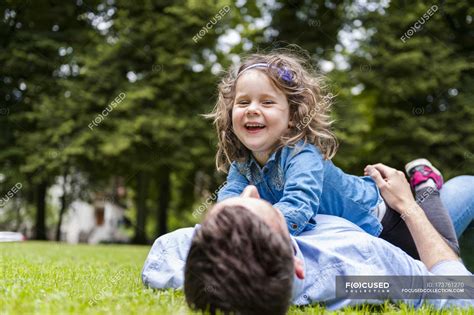 Father Cuddling With Daughter Lying On Meadow In Park Leisure