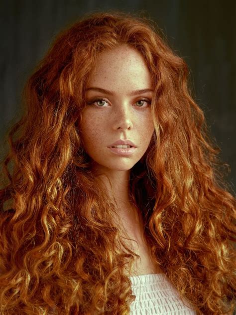 A Woman With Long Red Curly Hair Looking At The Camera