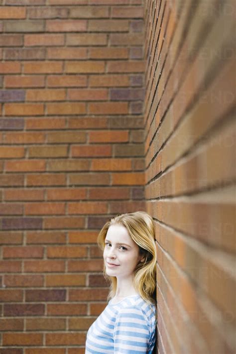 Portrait Of A Young Woman Leaning Against Brick Wall Stock Photo