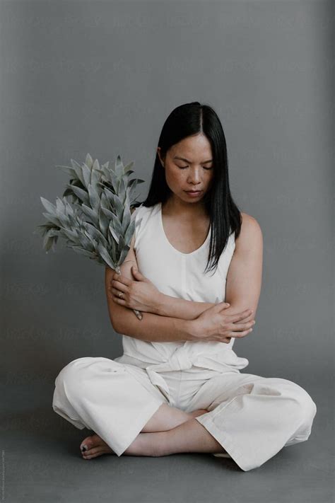Woman Sitting Cross Legged In All White Crossing Her Arms Holding Pale Green Plant By Stocksy