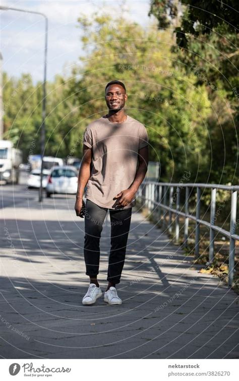 Young Black Man Walking On City Sidewalk A Royalty Free Stock Photo