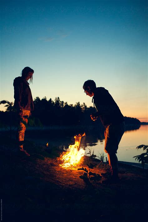 Two People Enjoying A Campfire Right Next To A Lake At Sunset By