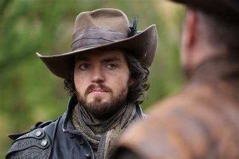 A Man With A Beard Wearing A Brown Hat And Leather Jacket Looking Off