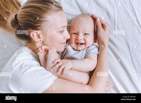 Top View Of Mother Cuddling Her Laughing Infant Baby In Bed Stock Photo