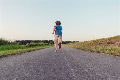 Boy Running Away On A Long Road In The Fields By Stocksy Contributor