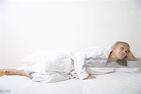 Young Woman In Bathrobe Looking Away While Lying In Bed On Her Side