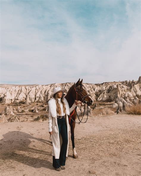 A Woman Standing Next To A Brown Horse On Top Of A Dirt Field With