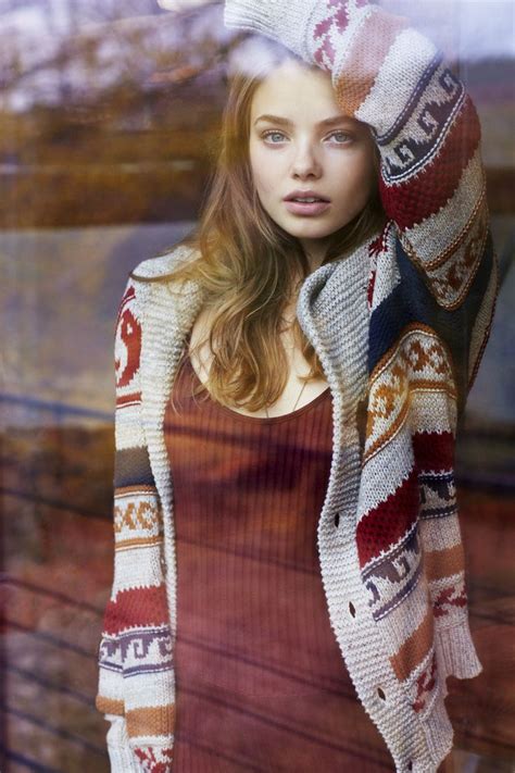 a woman is standing in front of a window with her hands on her head and wearing a sweater over