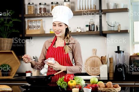 Happy Smiling Beautiful Asian Woman Wearing Apron And Chef Hat Adding