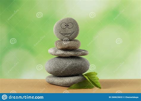 Stack Of Stones With Drawn Happy Face And Green Leaves On Table Against