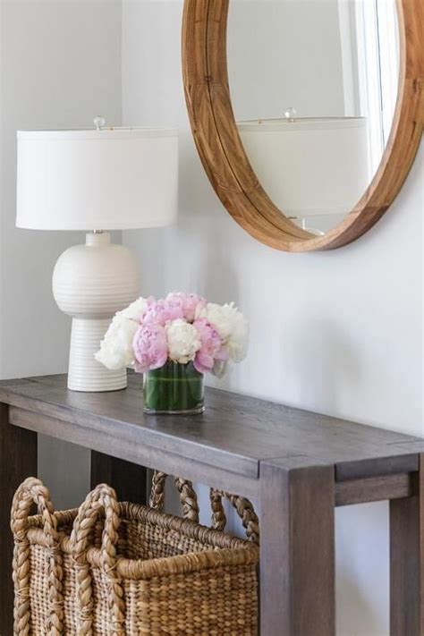 A Round Wood Mirror Stands Over A Brown Console Table Topped With A