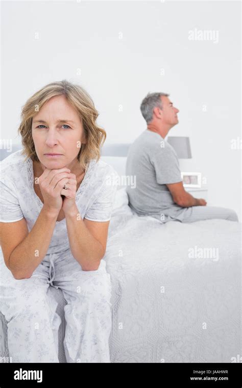 Fed Up Couple Sitting On Different Sides Of Bed Having A Dispute With