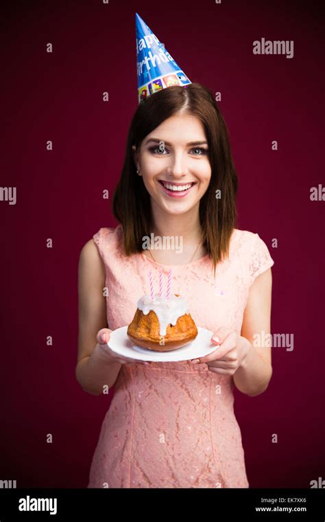 smiling pretty woman holding cake with candles over pink background looking at camera