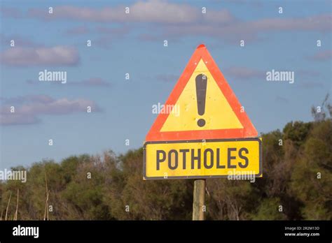Triangular Yellow Road Traffic Warning Sign For Potholes At The Side Of