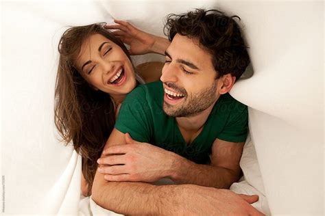 Young Carefree Couple Laughing And Enjoying Morning In Bed By Mosuno