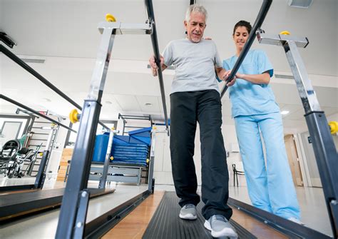 Occupational Therapist Helping Senior Patient On His Recovery Using Parallel Bars To Walk