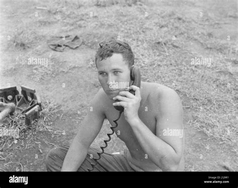 a shirtless united states soldier sits on the ground and speaks on a portable radio during the