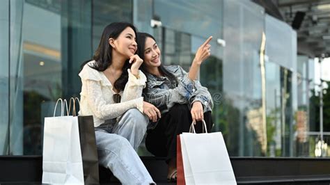 Beautiful Asian Women Friends In Trendy Clothes Sitting On Urban Stairs At The Shopping District