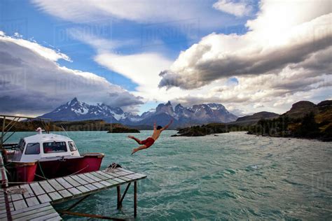 A Man Dives Off A Dock Into The Cold Waters Of A Turquoise Lake With A