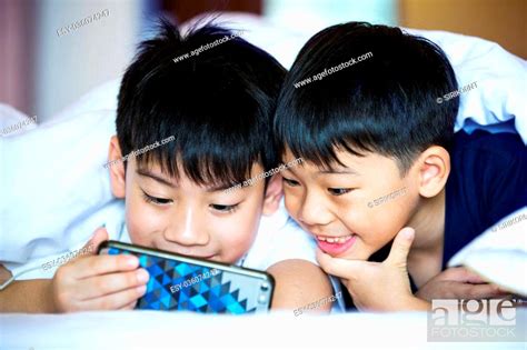 Asian Preschool Boys Playing On Smartphone Together Rest On Bed